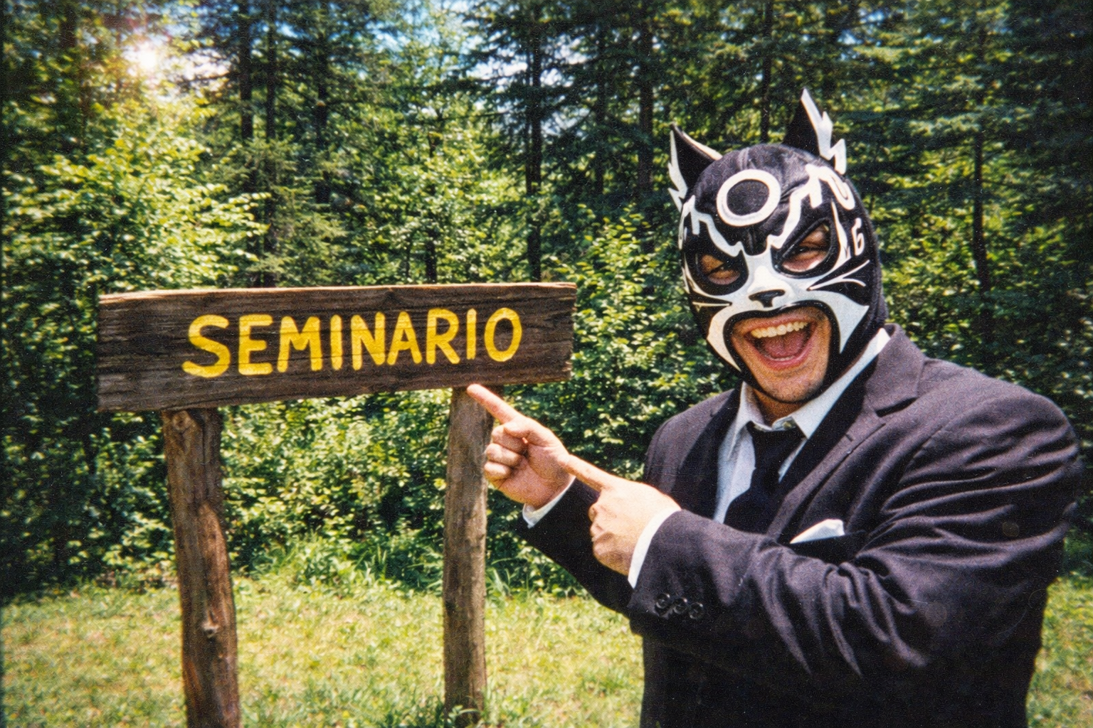 AI image prompt (360x240): A masked luchador standing beside a rustic wooden sign that reads 'SEMINARIO', pointing proudly, forest background, midday sun, cheap film camera, slight overexposure, late 90s vacation photo aesthetic.